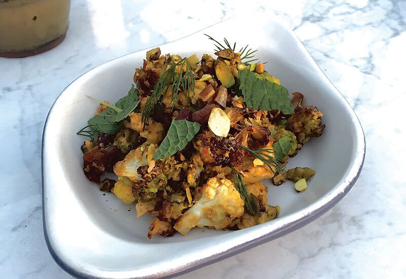 A starter like Charred Cauliflower, at True Food Kitchen, goes nicely with drinks. The dish has a kick and some texture from harissa tahini, dill, mint and pistachios.