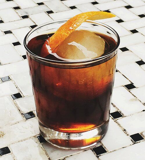 This Devil’s Reject cocktail gets a kick from Kraken Black Spiced Rum, applewood-smoked ice spheres and cardamom bitters, while flamed orange gives an extra caramelized aroma.