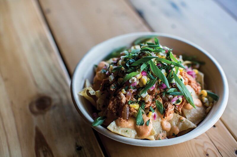 Fried Chicken Nachos fit seamlessly onto Honey Butter’s menu in Chicago, featuring fried chicken, pimento cheese, tortilla chips, lime crema, corn pico de gallo and candied jalapeño.