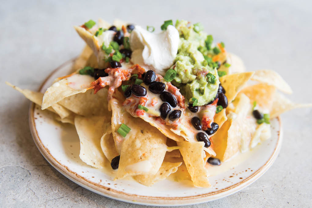 The Smoked Chicken Nachos at State Fare Kitchen & Bar, served on the happy hour menu, star guajillo smoked chicken, guacamole and sour cream.