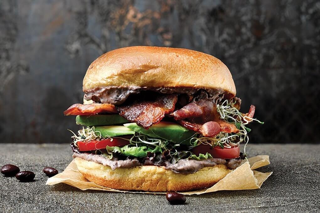 A black bean hummus (made with Bush’s Best Hummus Made Easy) is spread on a toasted brioche bun for a signature BLT sandwich.