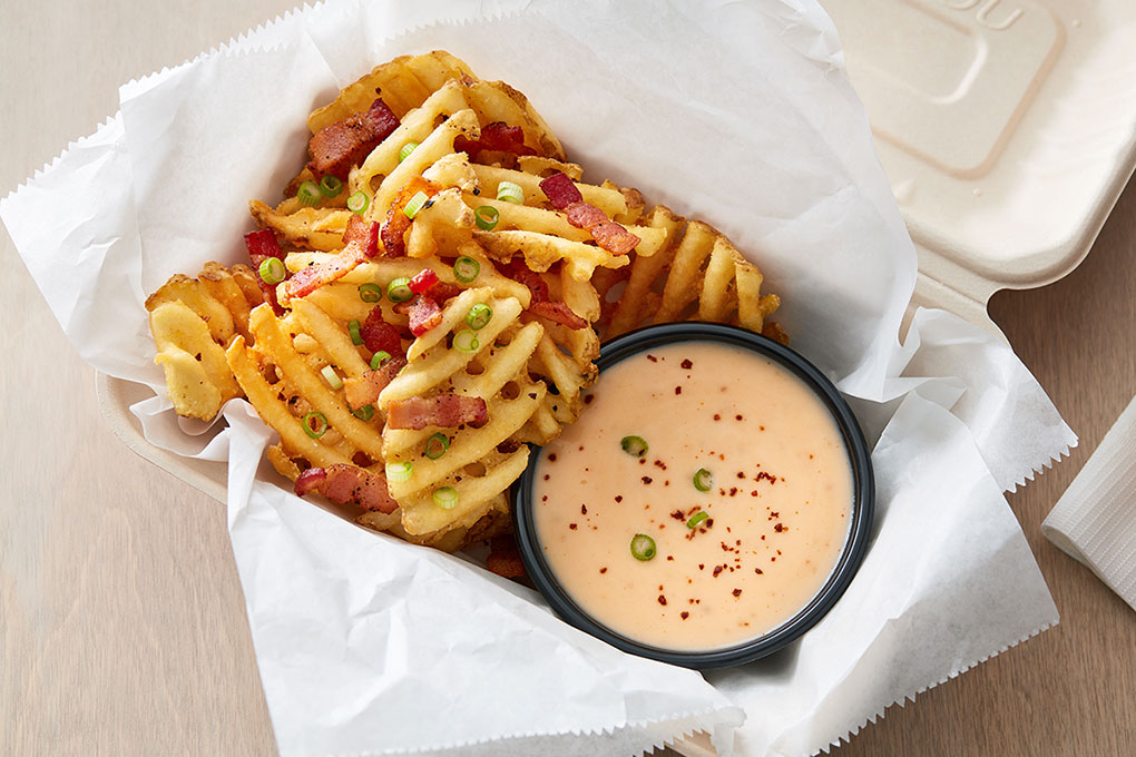 Waffle fries are the base in this craveable poutine-inspired build, with a warm, smoky, spicy cheese sauce topped with crisp bacon and green onions.