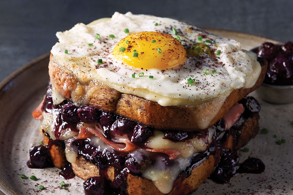 This Blueberry Croque Madame features French ham, Havarti, béchamel and a signature savory blueberry compote that balances the sweetness of the berries with rosemary, garlic, onion and balsamic vinegar. A crowning fried egg ensures breakfast or brunch positioning.