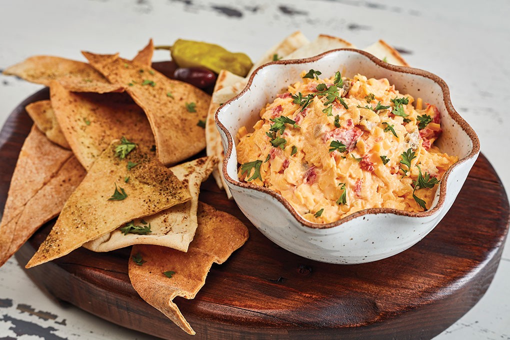 Taziki’s Mediterranean Café, a fast casual known for its Greek food, menus Spicy Pimento Cheese with pita and veggies, illustrating its broader acceptance outside of Southern-themed restaurants.