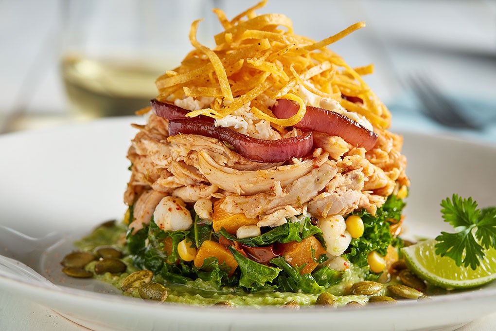 A Tomatillo Salsa Verde forms the base of a salad stacked with pulled chicken, balsamic onion rings, feta and crispy tortilla strips.