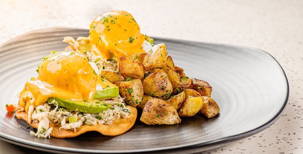 Crispy-fried white corn tortillas topped with refried beans, smashed avocado, crab salad and a soft-poached egg, finished with chipotle hollandaise, served with papas rancheras