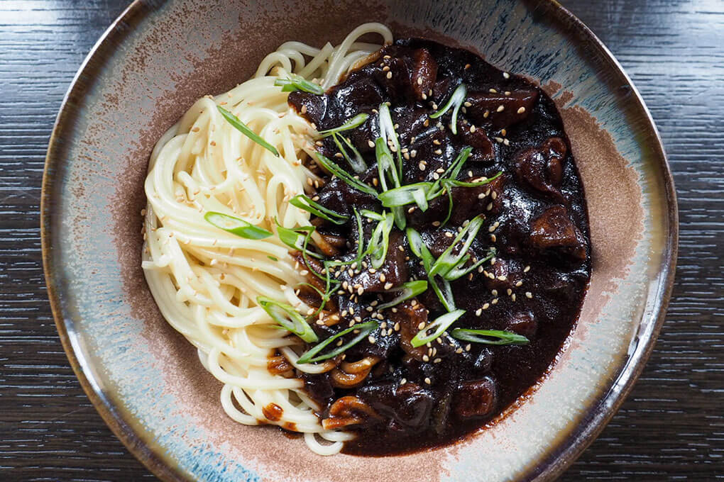 Korean JJ Noodles with crispy pork belly, onions, potatoes, zucchini and fermented black bean paste