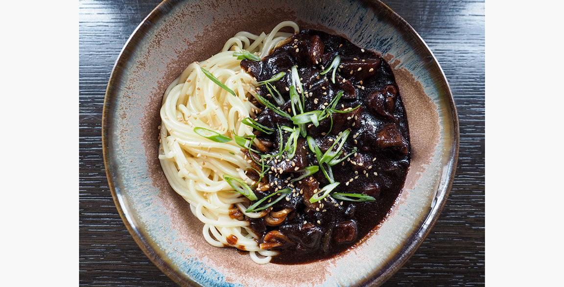 Korean JJ Noodles with crispy pork belly, onions, potatoes, zucchini and fermented black bean paste