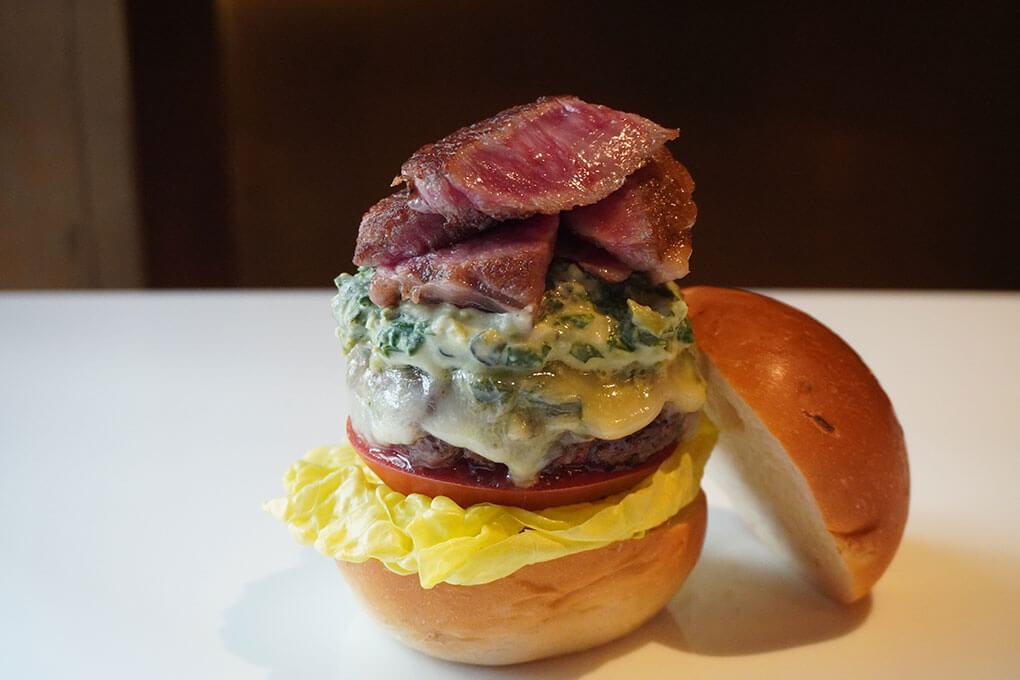 Waygu beef patty and steak slices, wasabi leaf, béchamel, Gorgonzola, provolone, housemade sansho pepper sauce, beefsteak tomato, Boston lettuce and steak-truffle salt on an onion bun