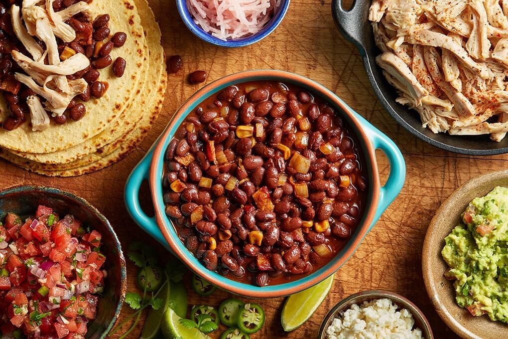 Dave Woolley developed this fun taco spread featuring mole-inspired Bush’s Fiesta Beans layered with chiles and chocolate, smoky shredded chicken, pico de gallo, pickled jicama, sour cream and “street corn” guacamole.