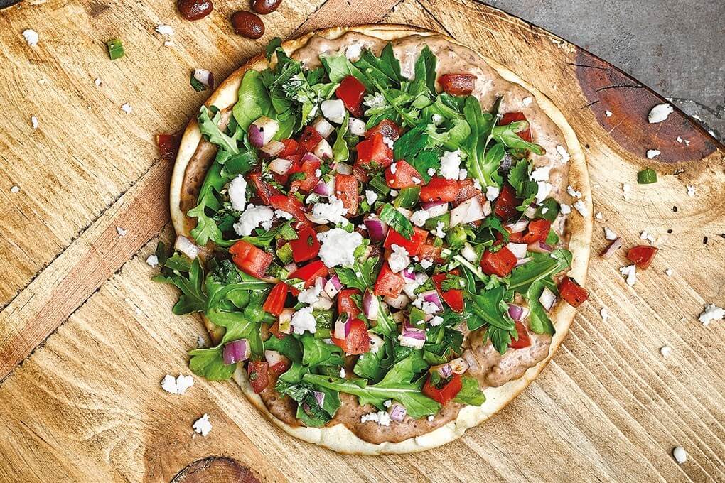 In this Taco Fiesta Hummus Flatbread, Bush’s Best® Easy Entrées® Taco Fiesta Black Beans and hummus are puréed, creating a delicious Mediterranean-Mexican mash-up as the base. Queso fresco, pico and arugula round out the look.