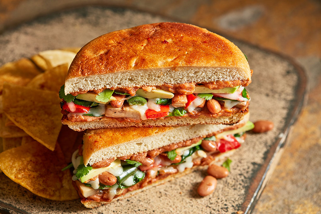 Chef Jeff Mann builds this rich, veg-friendly torta from a Telera roll toasted with Chipotle Butter, smashed Ranchero beans and roasted vegetables